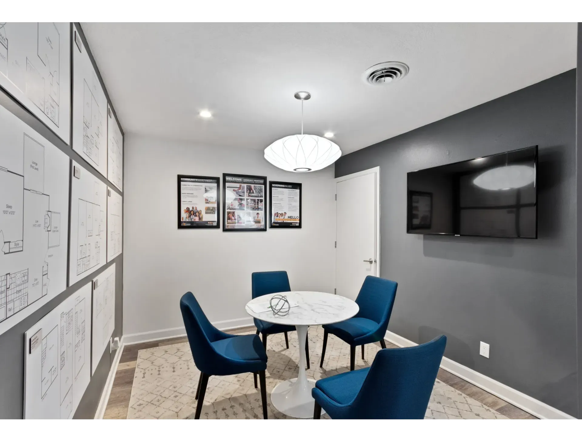 Meeting room with blue chairs and a round table, featuring floorplan diagrams on the walls.
