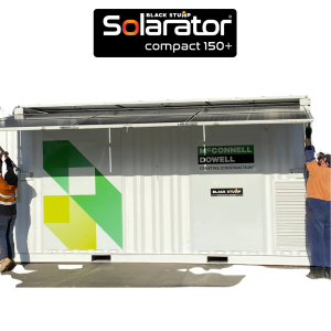 Two workers lifting a Solarator compact 150+ unit, a container-like solar power generator. White container with green and yellow logo.