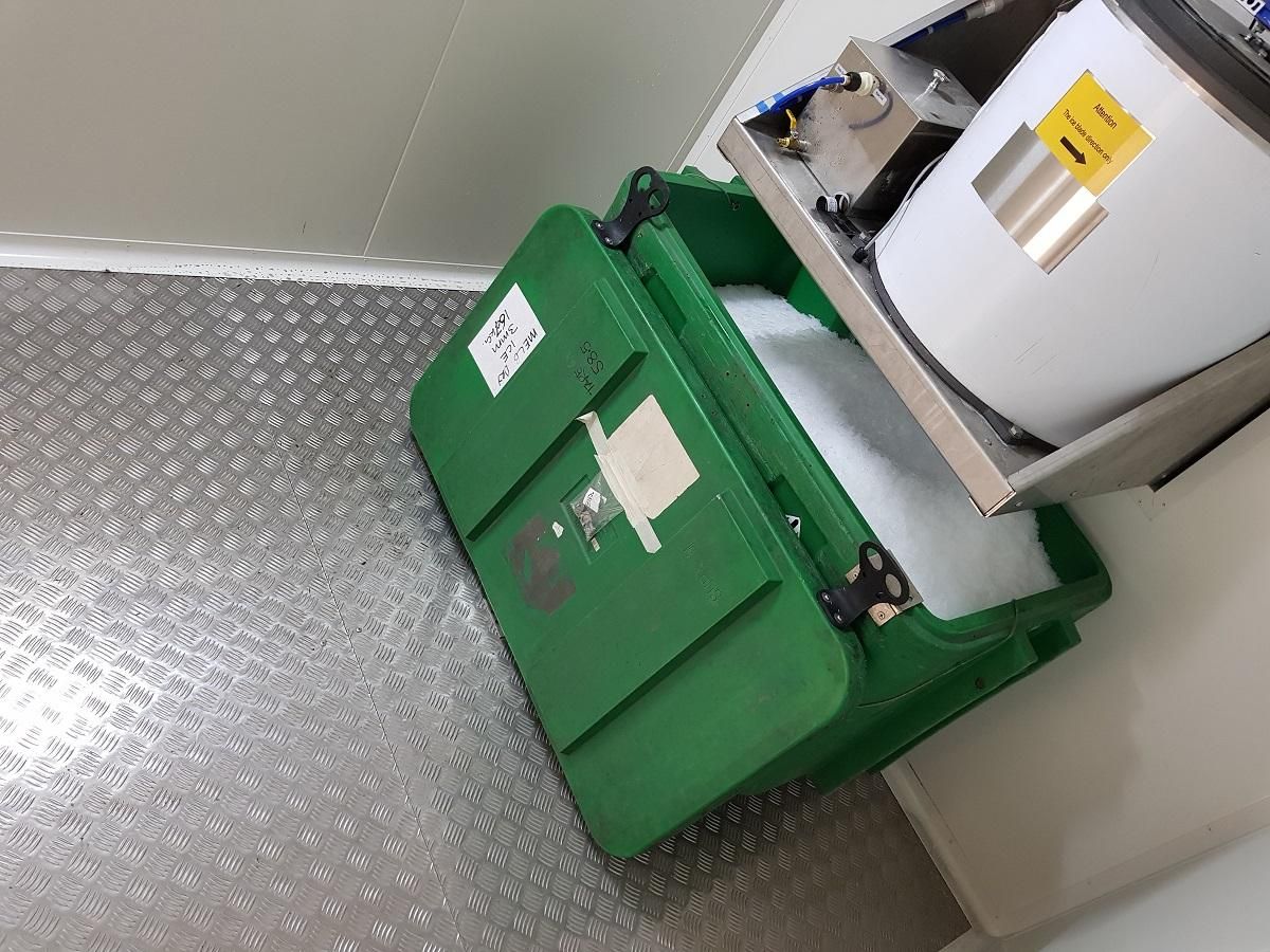 Green bin open with white foam inside next to a silver appliance and metal flooring.