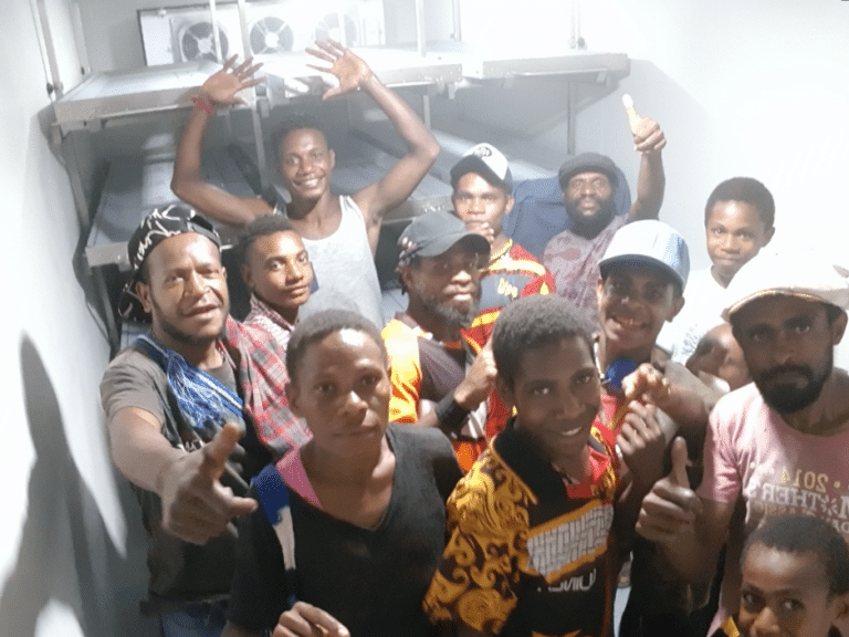 Group of people indoors smiling and gesturing with thumbs up and arms raised.