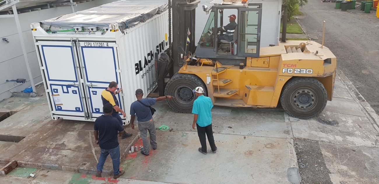 A forklift moving a shipping container with workers present.