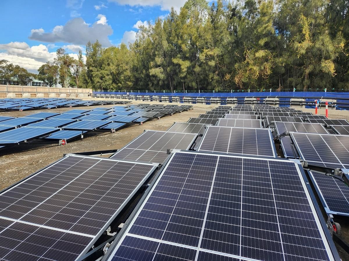 Solar panels in a field, trees in the background. Blue sky with clouds.