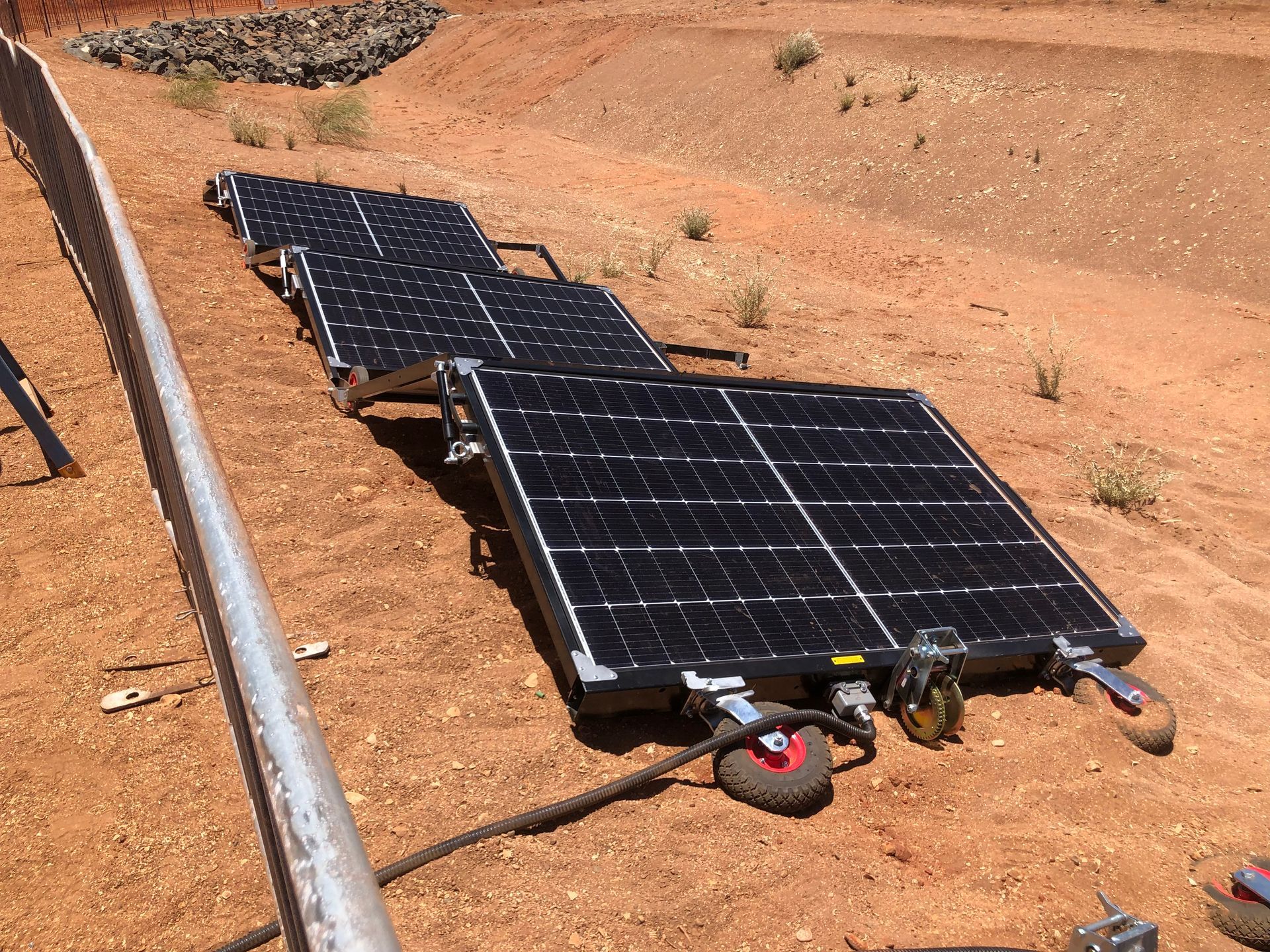 Solar panels on wheels in a red dirt area.