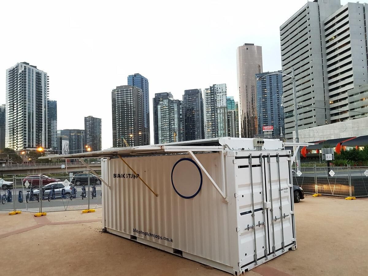 White shipping container kiosk with awning, circle cutout, and city skyline backdrop.