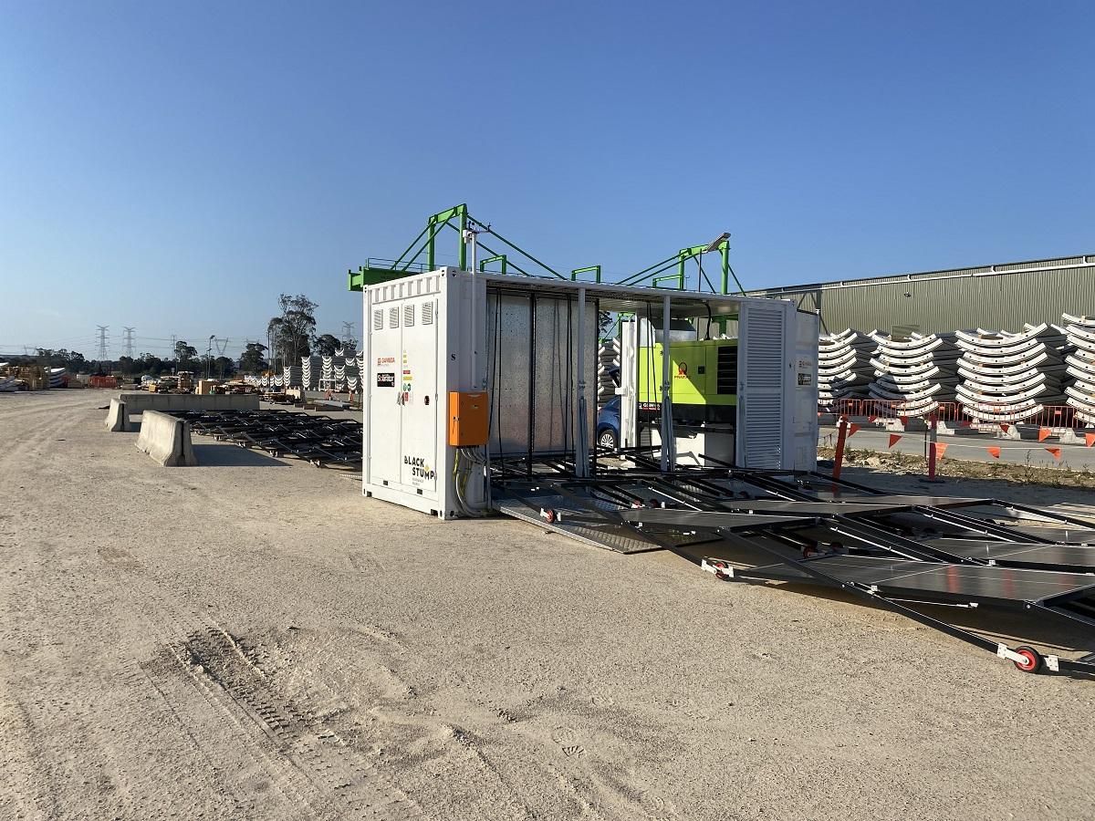 Large industrial machine outdoors on a gravel lot. White and green metal structure with extending platforms, bright blue sky.