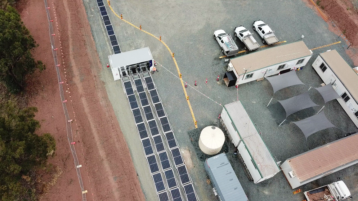Aerial view of a solar panel array powering a construction site with portable offices, vehicles, and water tank.