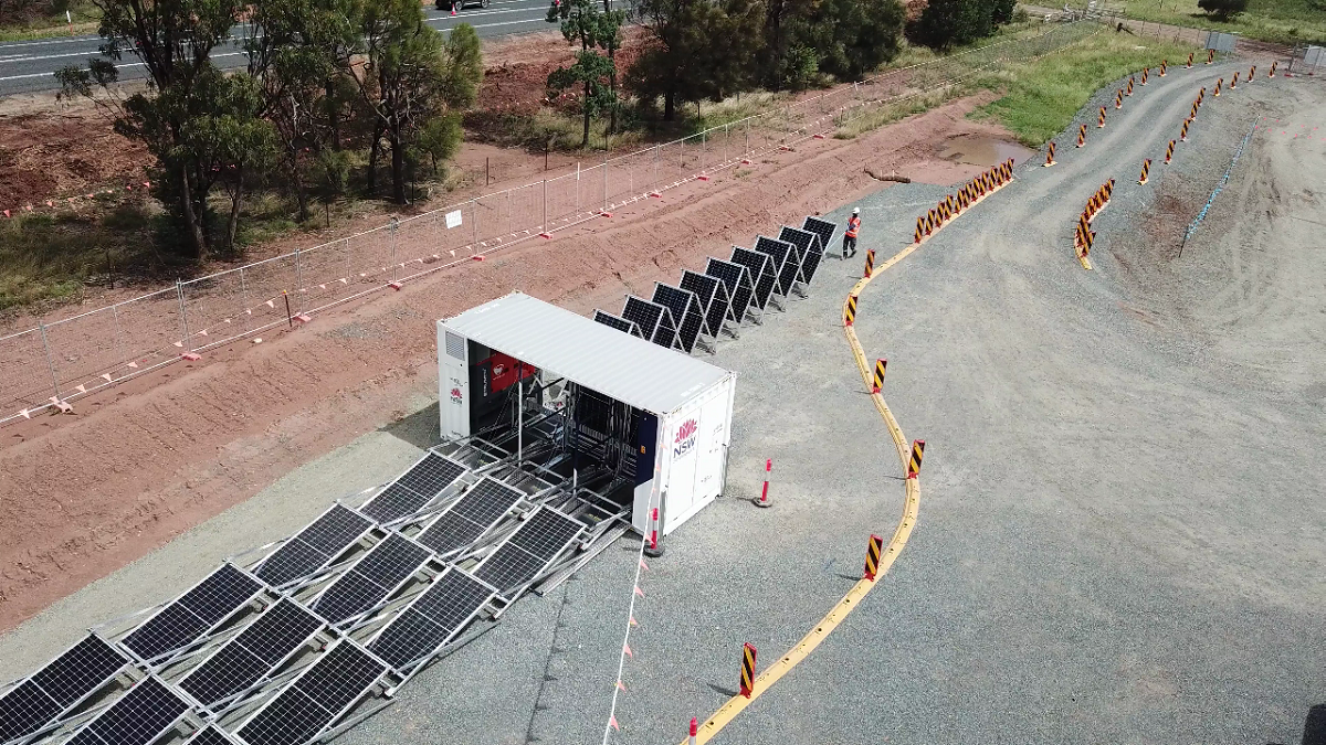 Solar panels powering a container with chairs set up. Person walks toward seats. Outdoors on gravel.