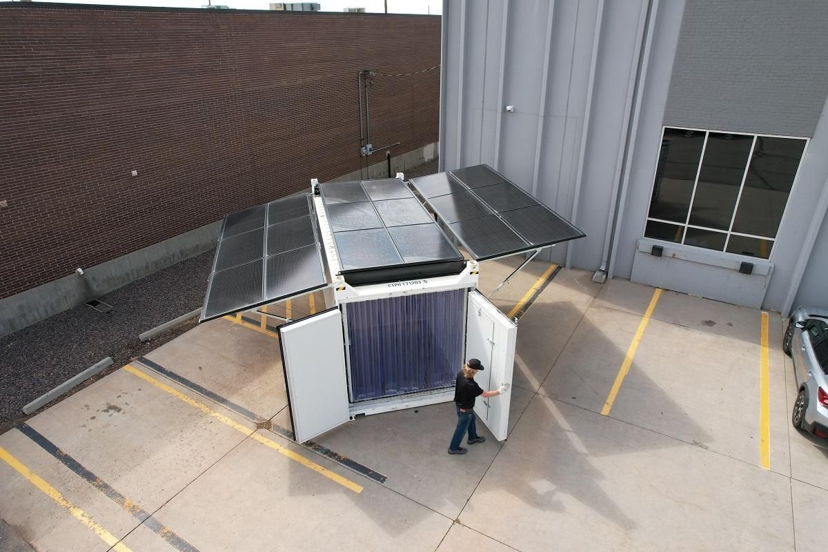 Overhead view of mobile solar power unit with open doors, person adjusting interior. Exterior setting.