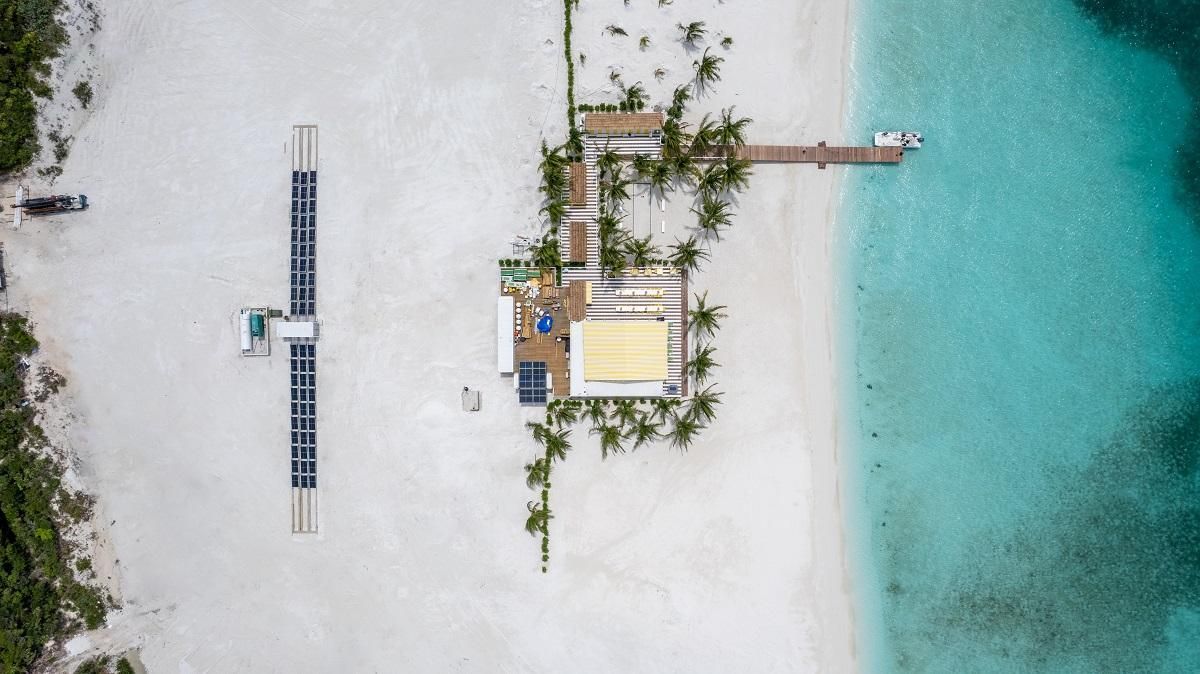 Aerial view of a beach resort with solar panels, a pier, white sand, and turquoise water.