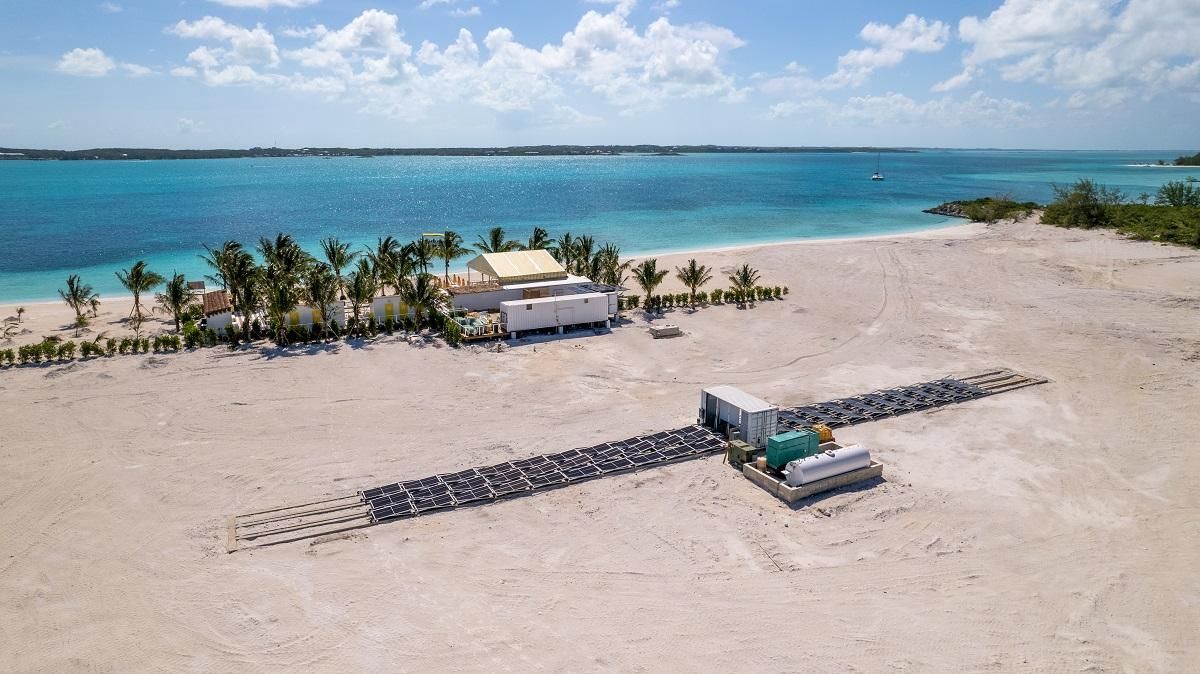 Aerial view of a white sandy beach with turquoise water. Buildings and palm trees are present.