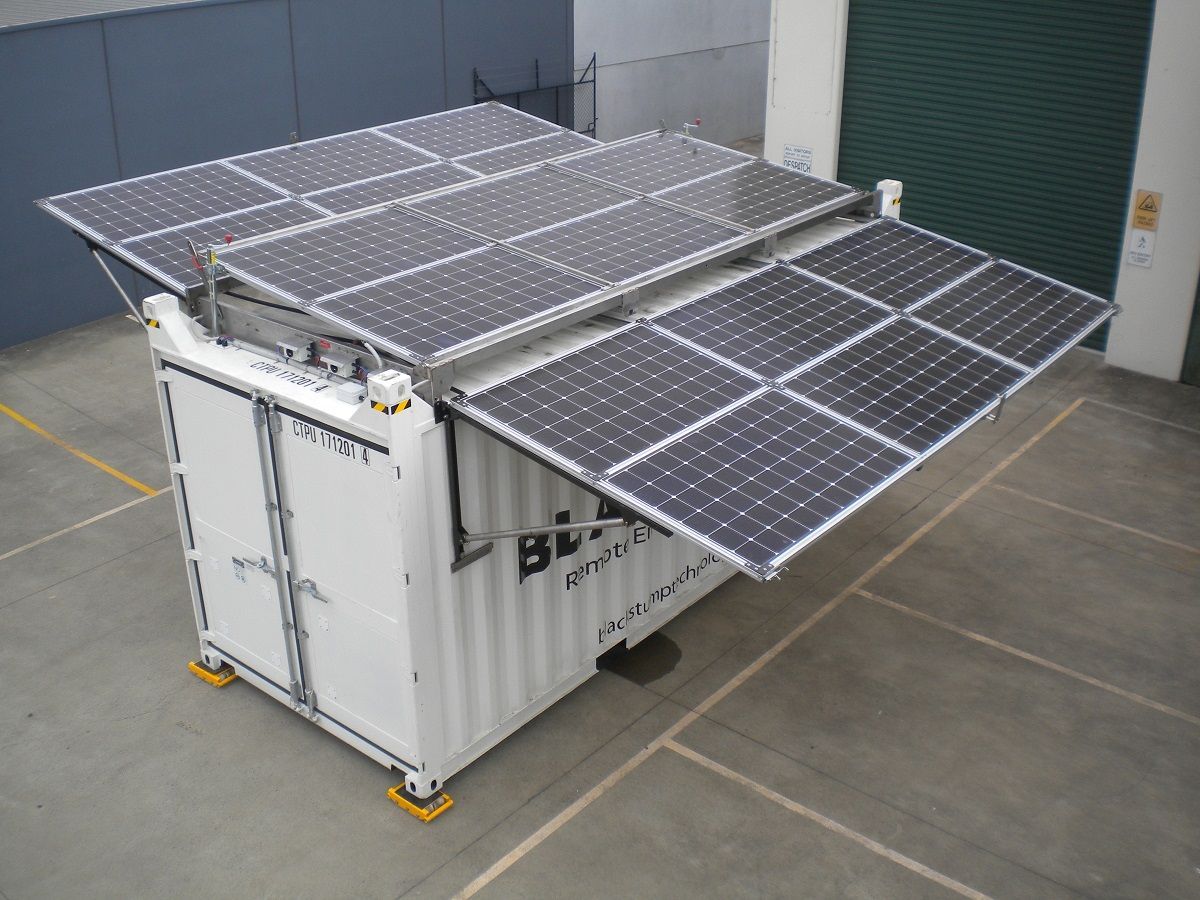 White container with deployed solar panels; indoors, gray floor.