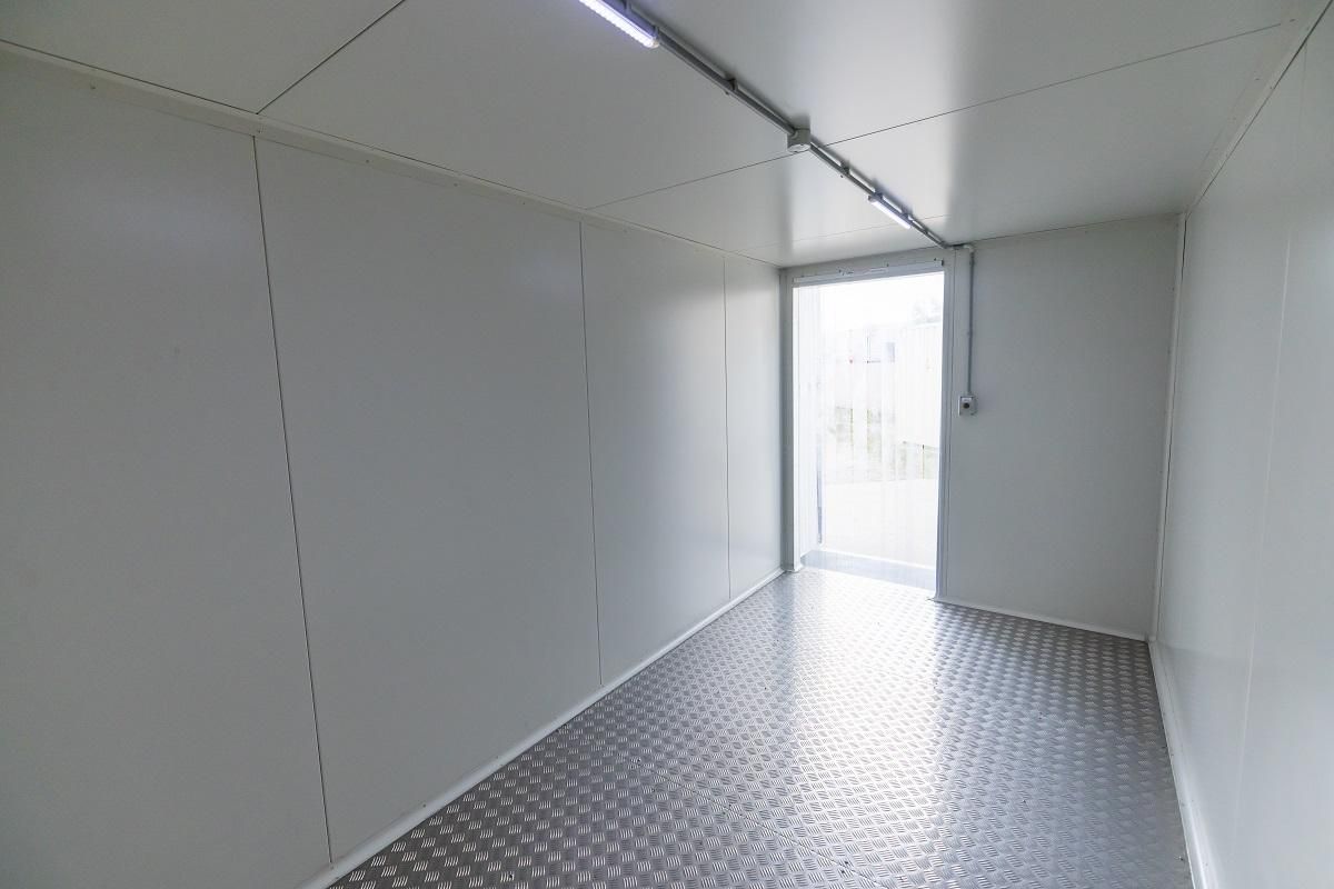 Empty, rectangular interior with white walls, metal floor, and a door at the end.