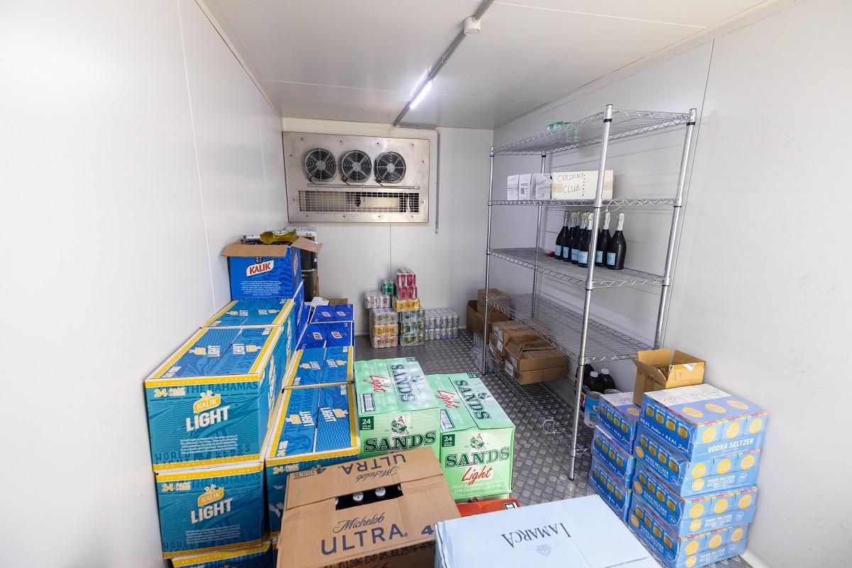 Interior of a cold storage room filled with stacked boxes of beer and shelving units with bottles.