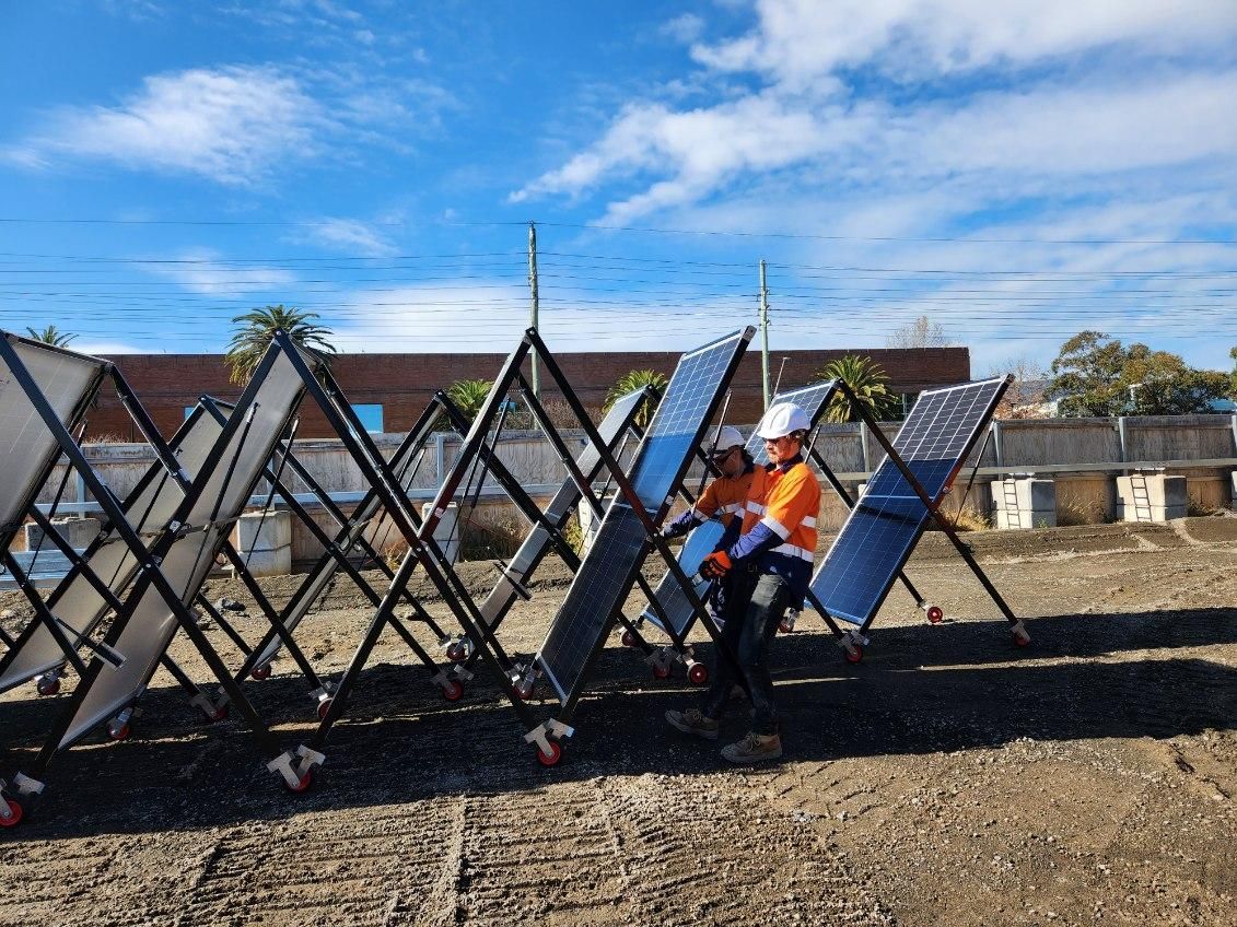 Two workers installing portable solar panels in an open area. Blue sky in background.