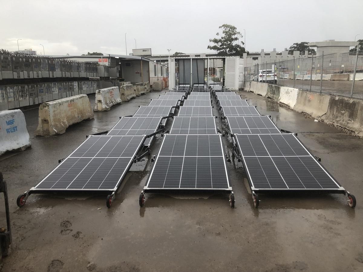 Solar panels on wheels in a wet outdoor setting, surrounded by concrete barriers.