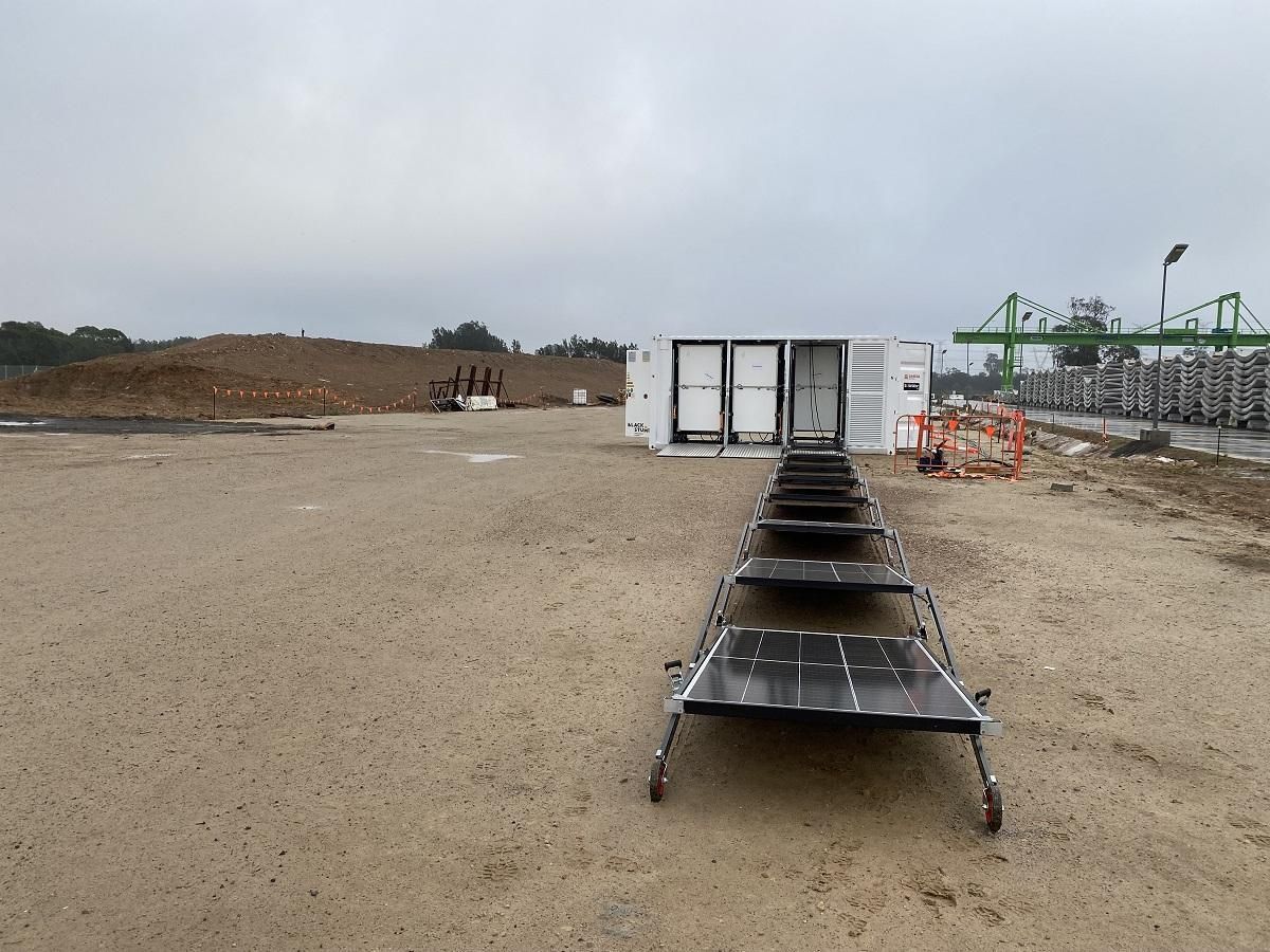 A container with open doors and a ramp in a dirt lot under an overcast sky.
