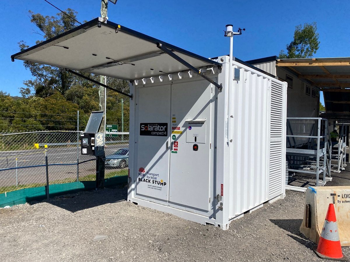 White container with an open awning and attached equipment, outdoors, likely a monitoring station.
