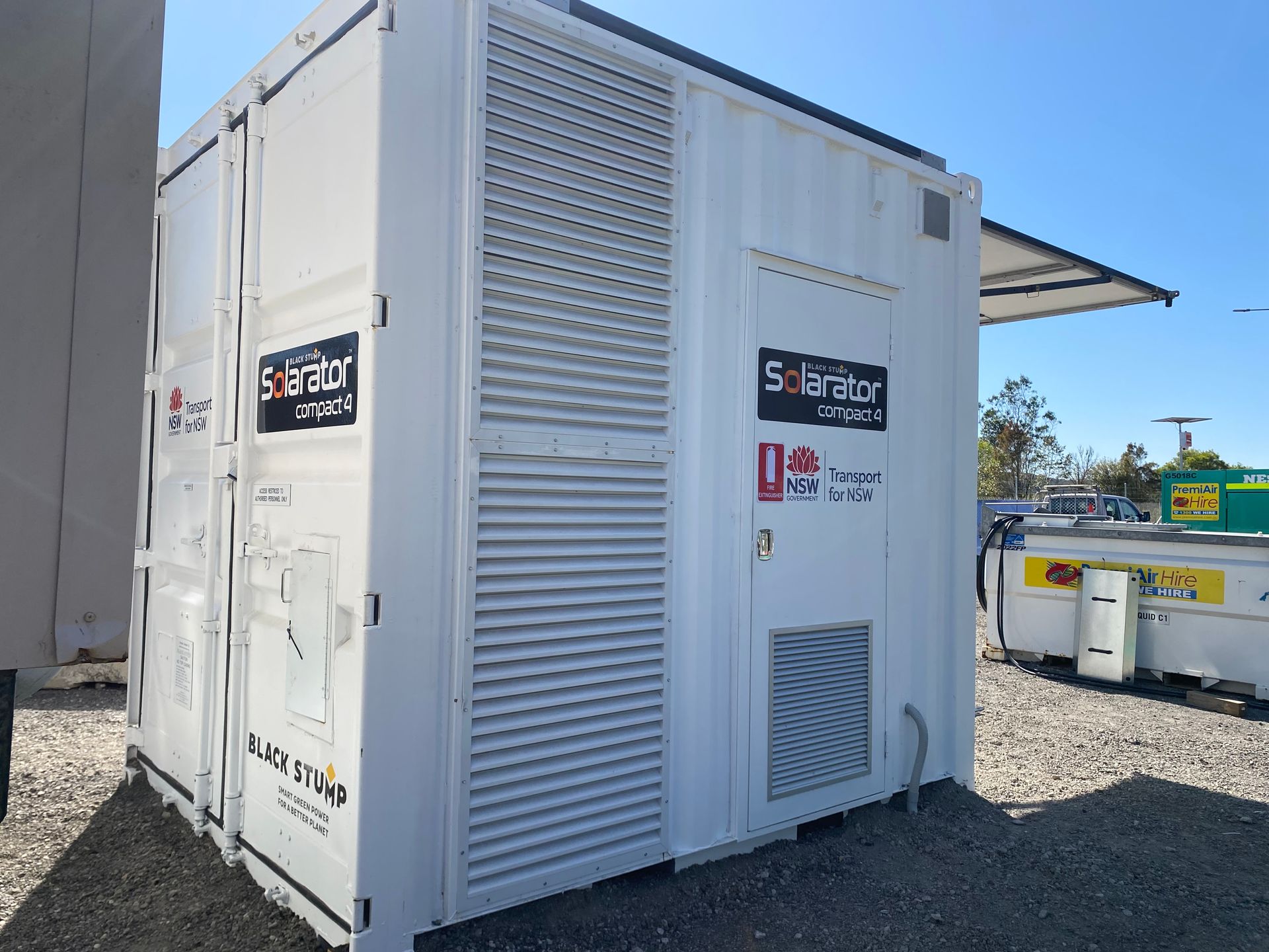 White industrial generator container with vents, logos, and a side door, outdoors in daylight.