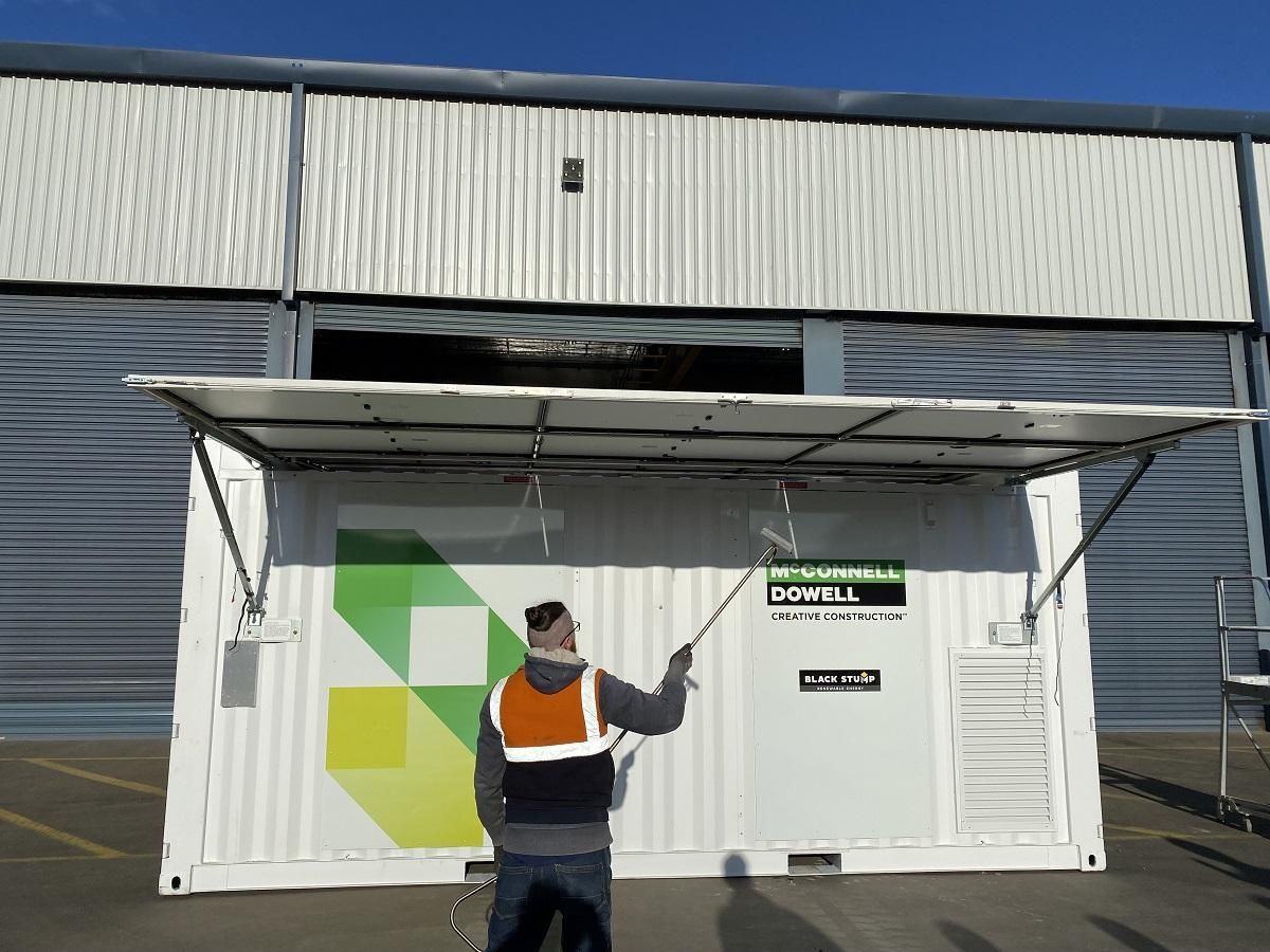 Man spraying container with awning in front of a building.