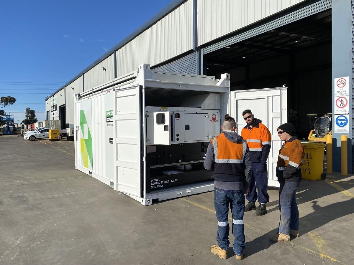 Workers examining machinery inside a white container with BP logo. Outside, a sunny day at a factory.