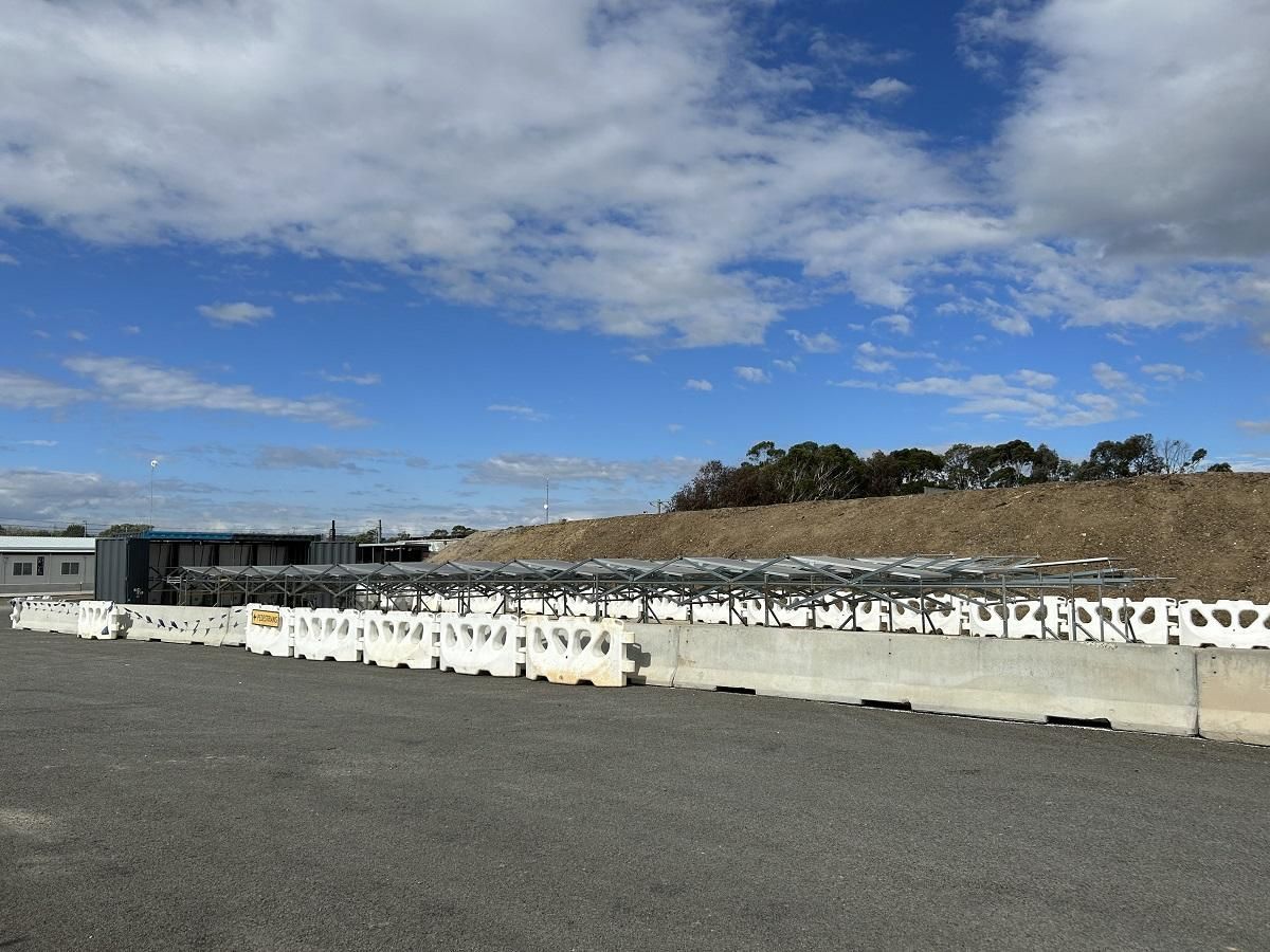 Solar panel array behind concrete barriers under a partly cloudy sky.