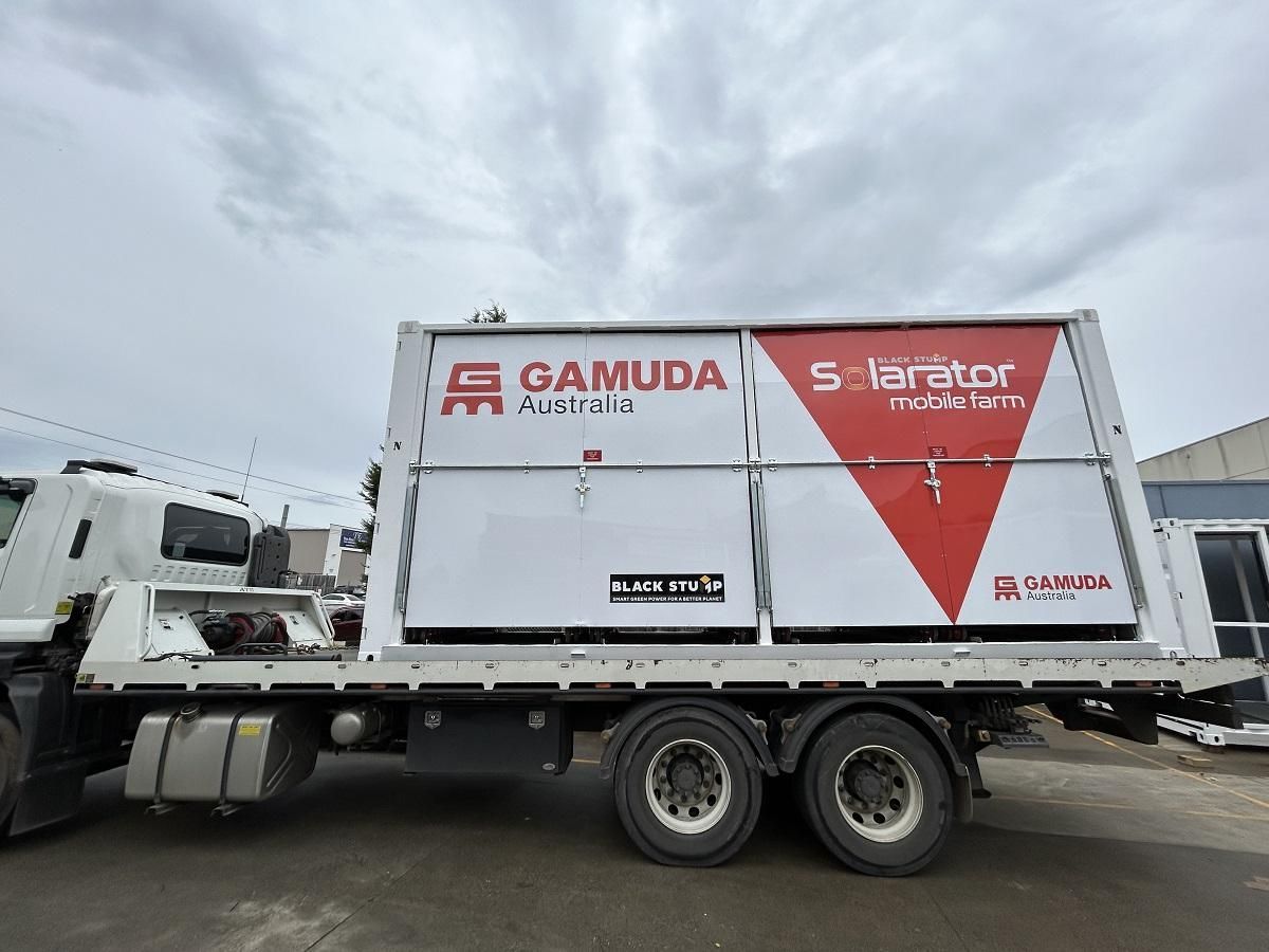 White truck with Gamuda Australia sign, carrying a red and white 5 Tarator unit, parked outside.