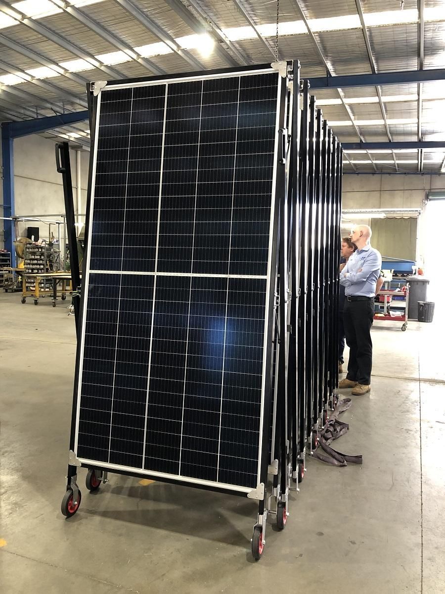 Solar panels on wheeled frames inside a factory; a person stands nearby.