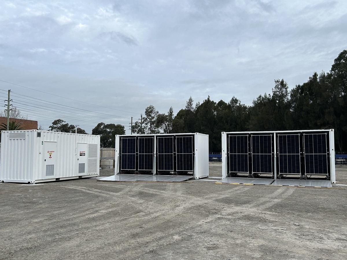 Three white container units on gravel, likely for power storage, under overcast sky.