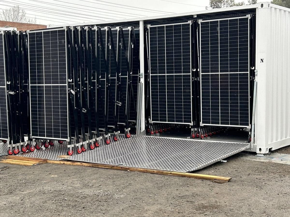 Solar panels on wheels emerge from shipping container, ramp extends to ground.