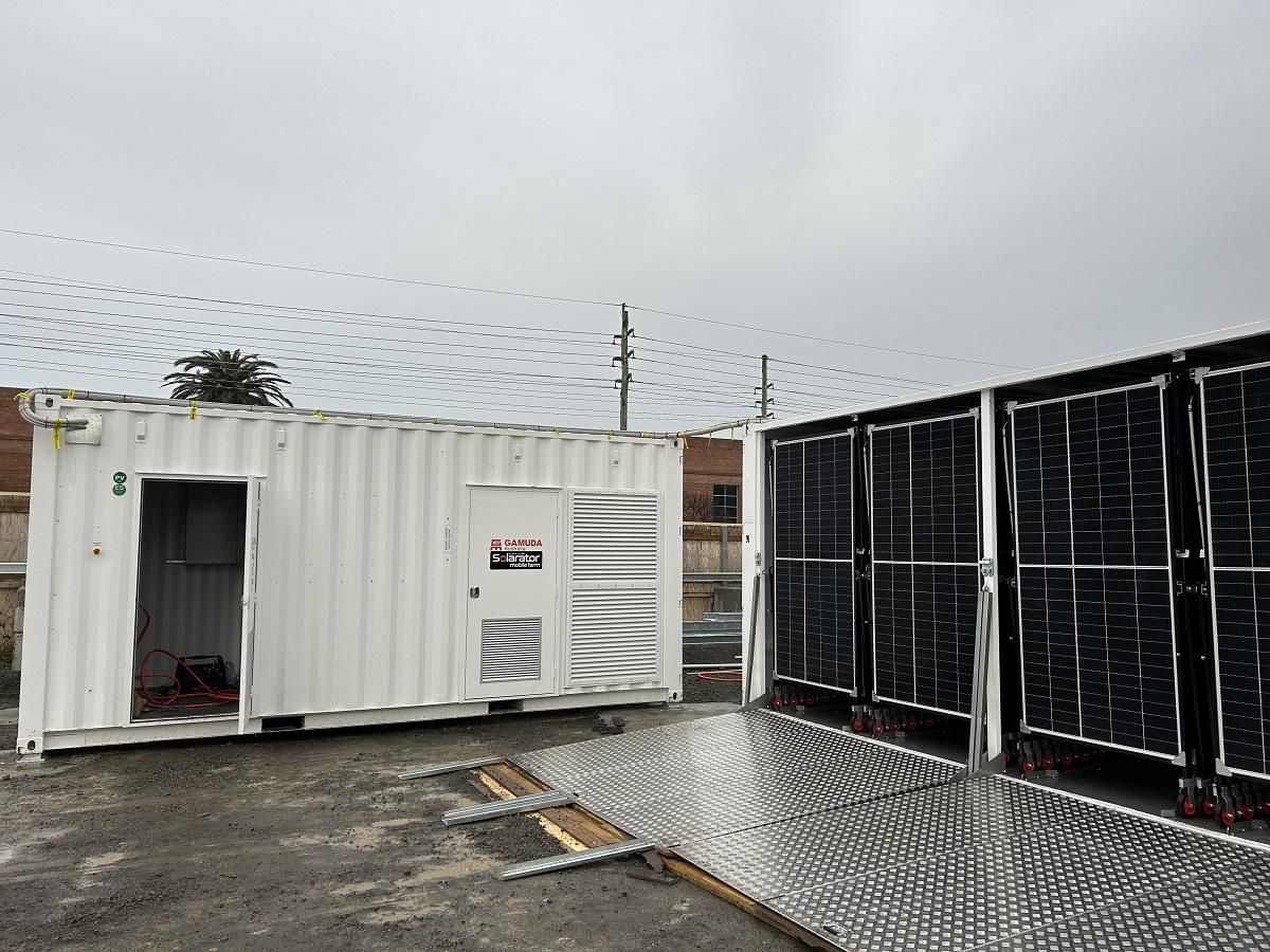 White container next to solar panels on a gray surface, cloudy sky overhead.