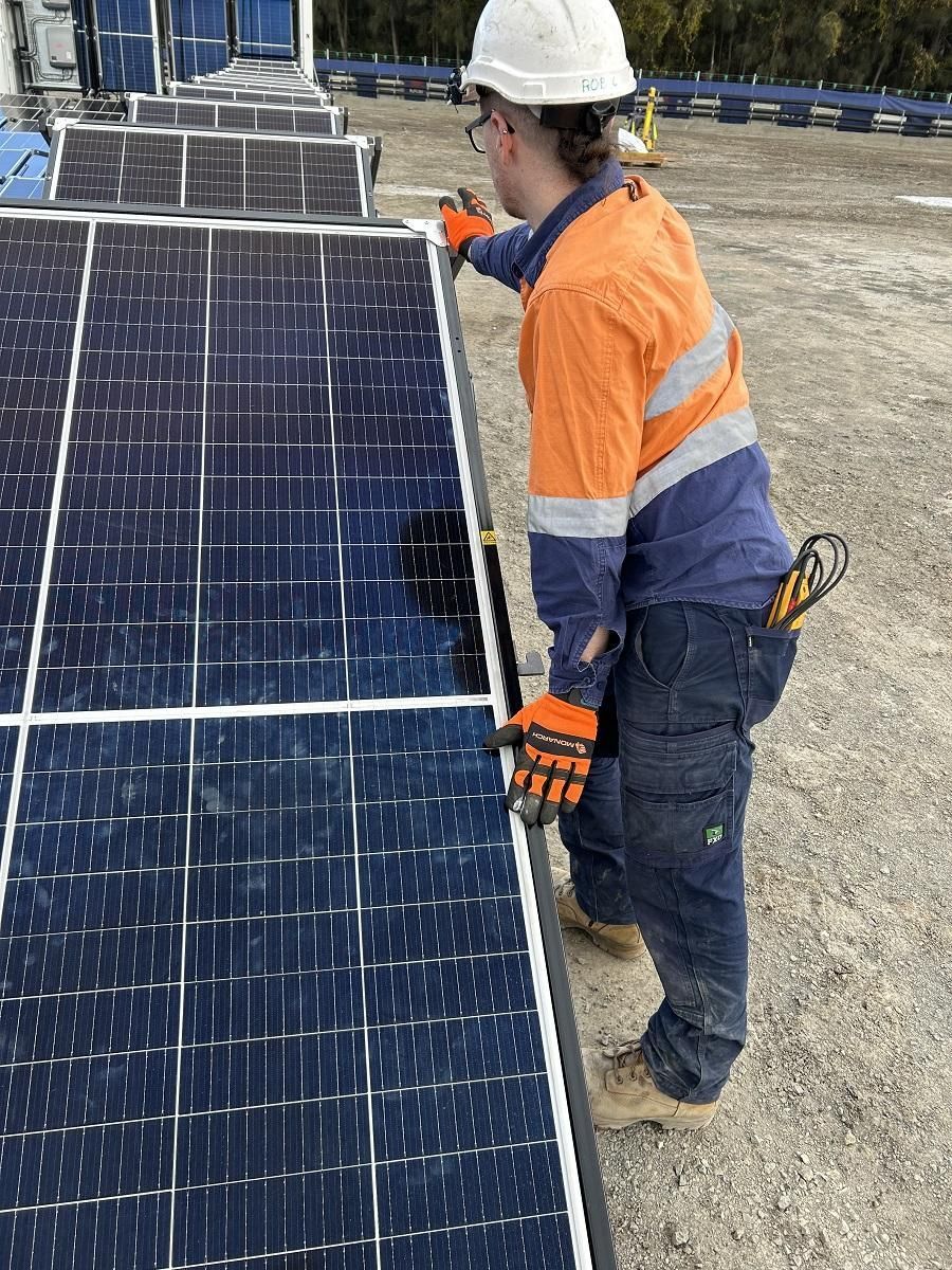 Solar panel installer in an orange and blue work shirt and hardhat, working on solar panels outdoors.