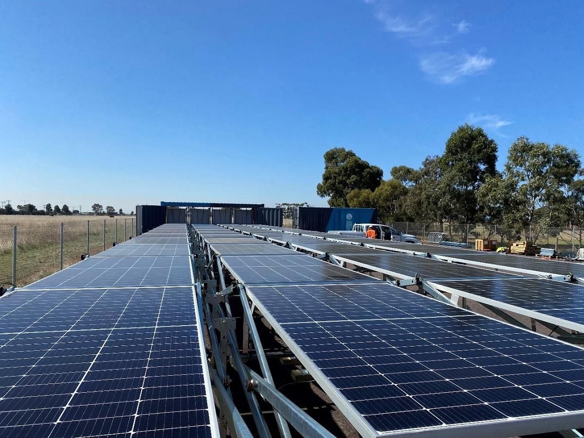 Solar panels arranged in rows under a clear blue sky, next to a fenced field.