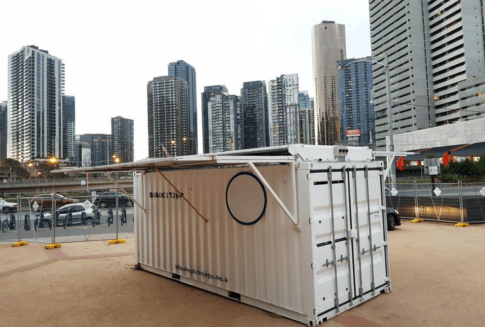 White shipping container with a retractable awning, in front of city skyscrapers.