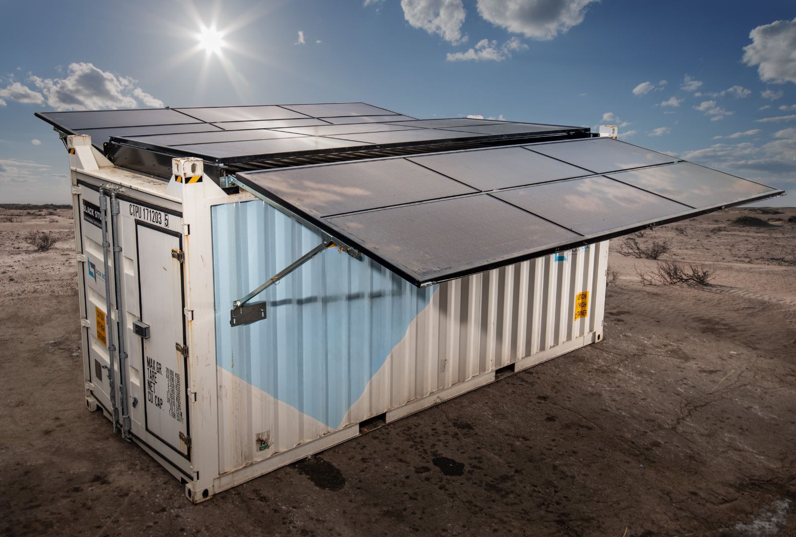 Shipping container with solar panels angled outward in a desert setting under a bright sun.