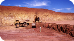 Earthmoving machinery, including a dump truck and excavator, in a reddish-brown open-pit mine.