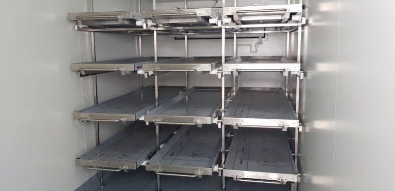 Interior of a refrigerated mortuary, with multiple stainless steel body storage shelves.