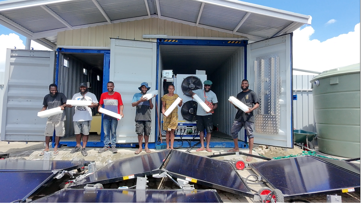 Group of people with rolled papers by solar panels and a container building.