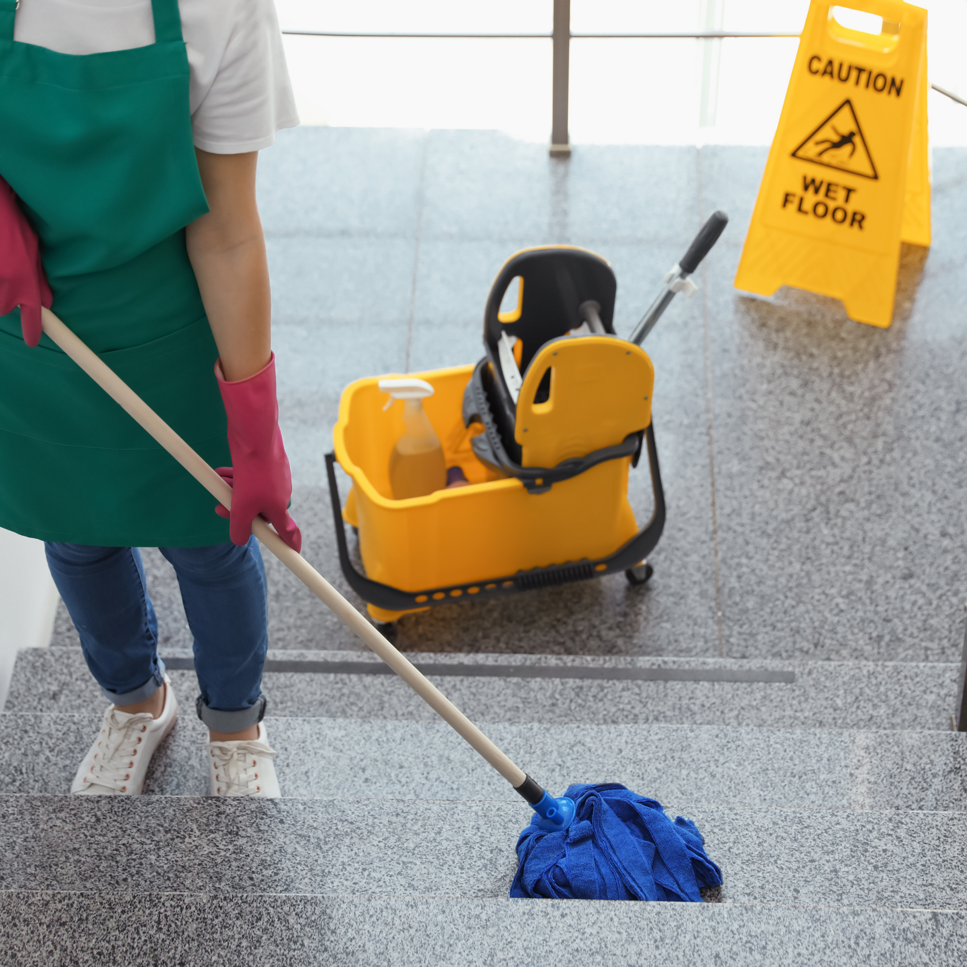 Person mopping stairs with cleaning supplies; caution wet floor sign nearby.