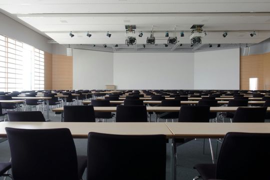 Empty conference room with rows of tables and chairs facing a large screen.