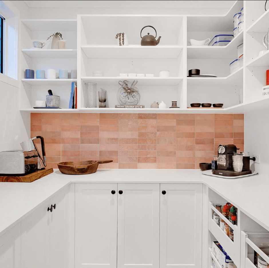 A kitchen with white cabinets , shelves , and a brick wall.