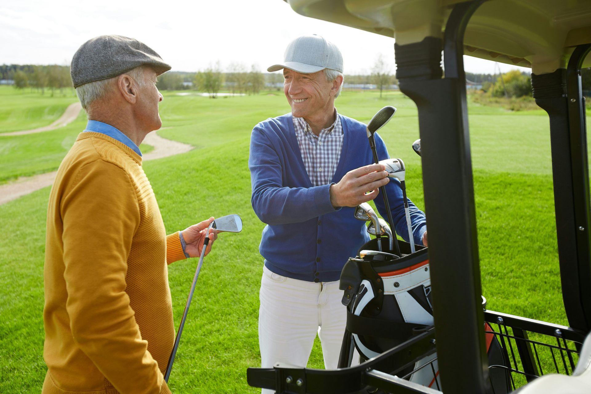 Two men are standing next to a golf cart on a golf course.