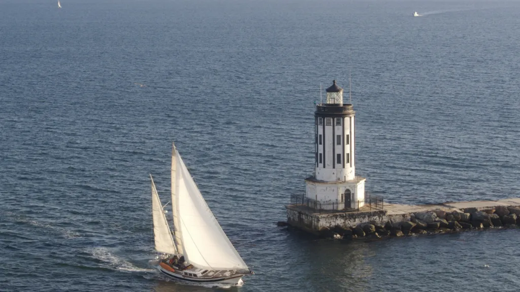 A sailboat is passing a lighthouse in the ocean