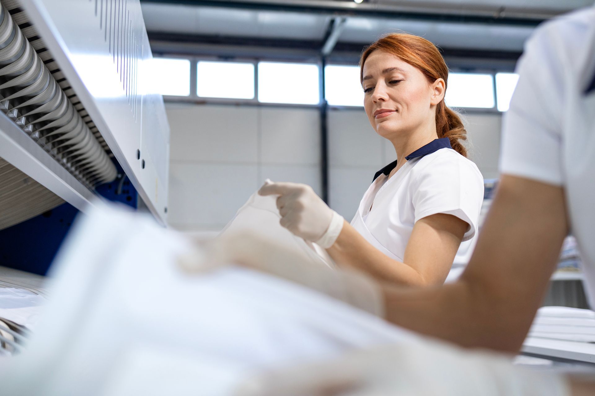 Woman in white uniform sorting linens in a laundry facility, wearing gloves, smiling.