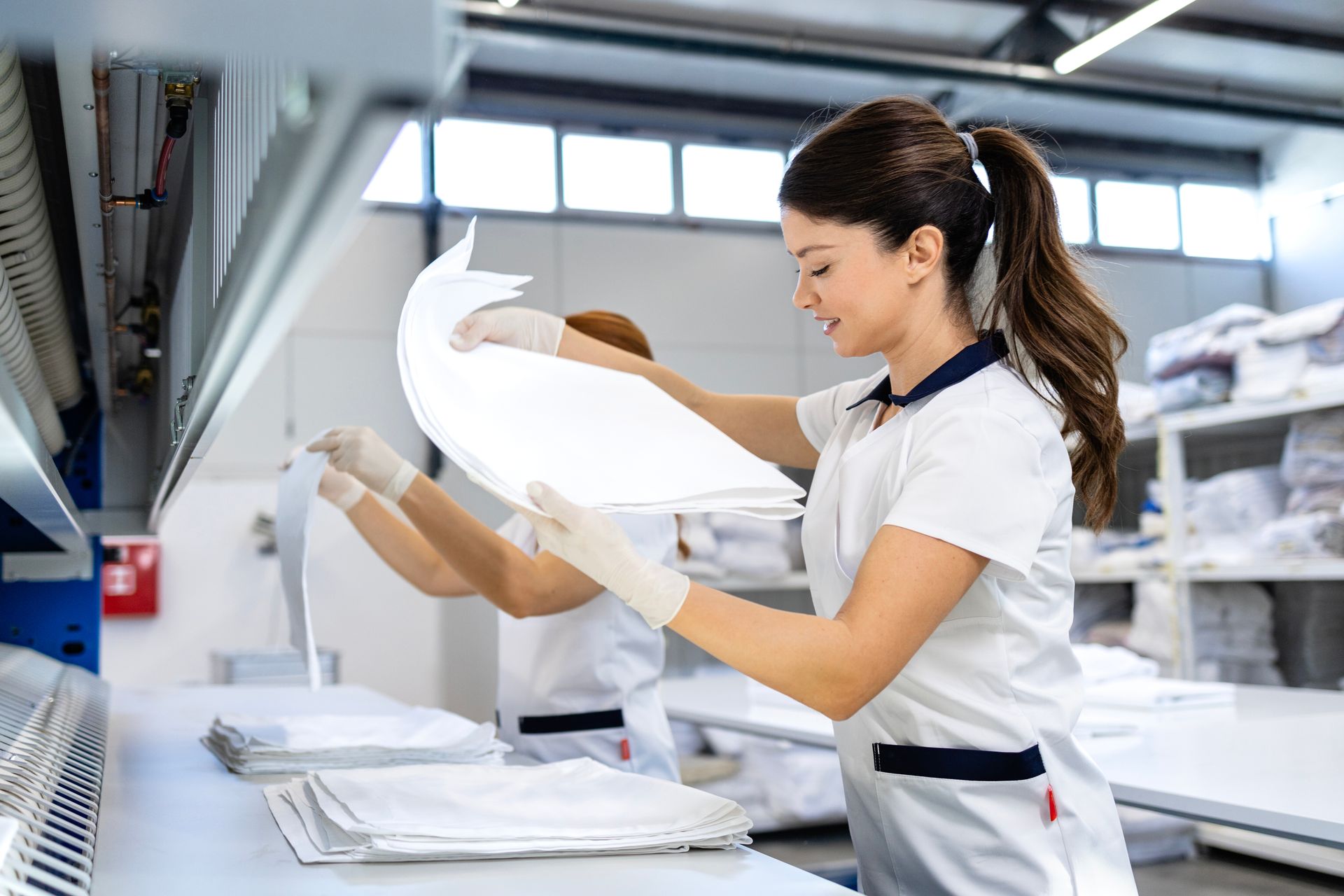 Two workers in a laundry facility folding clean, white linens.
