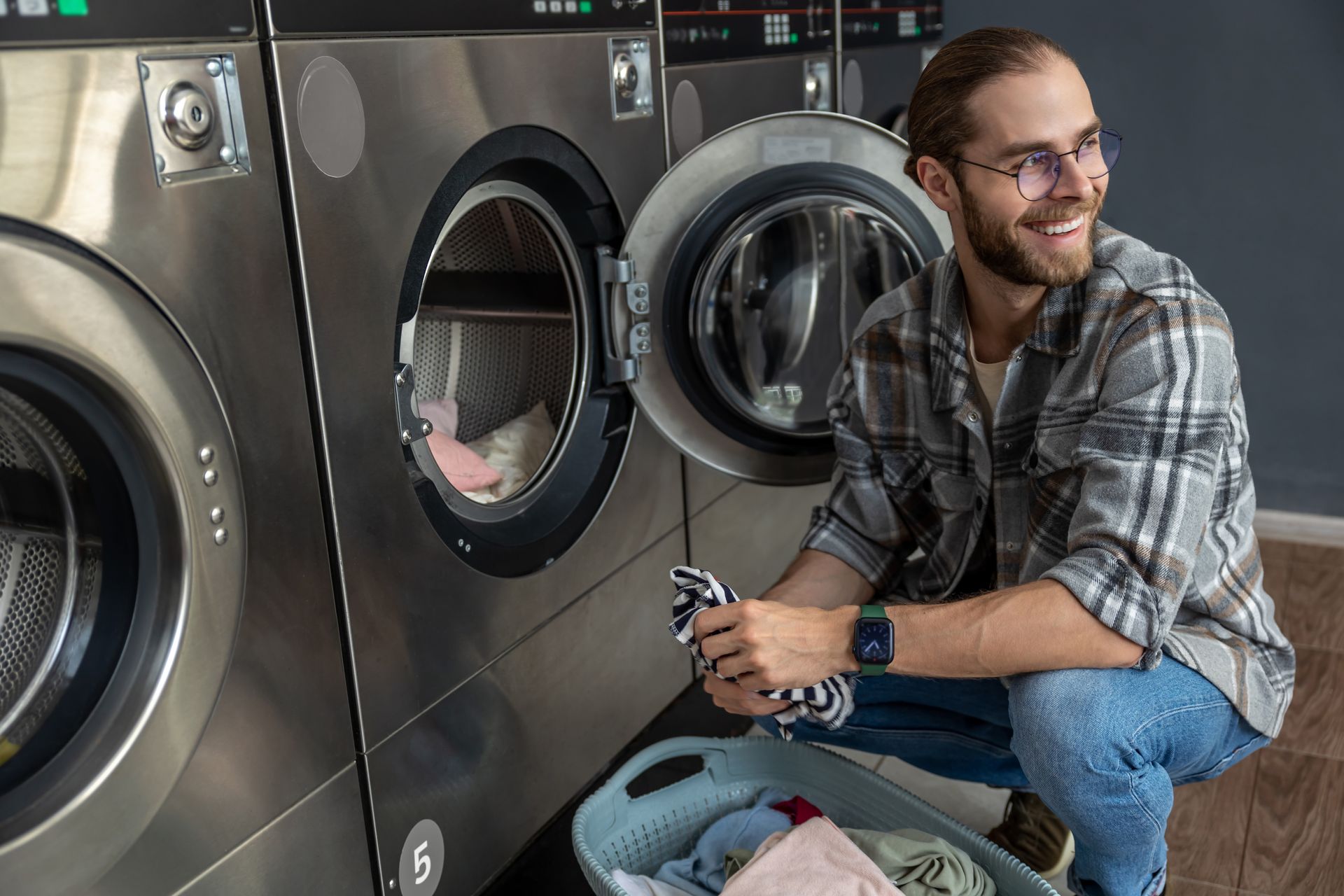 Man smiling, loading laundry into a washing machine at a laundromat.