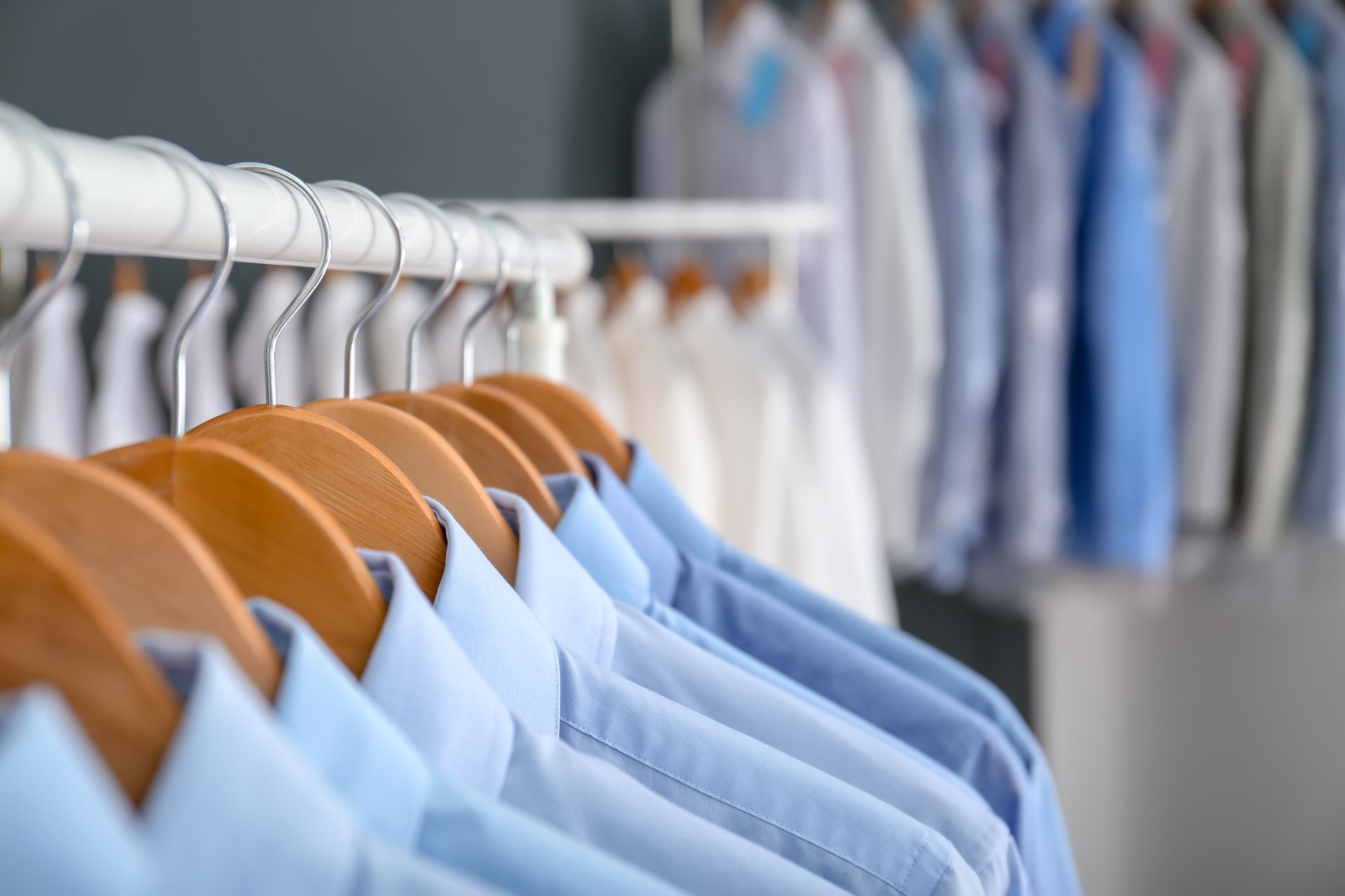 Light blue and white shirts hanging on wooden hangers on a rack.