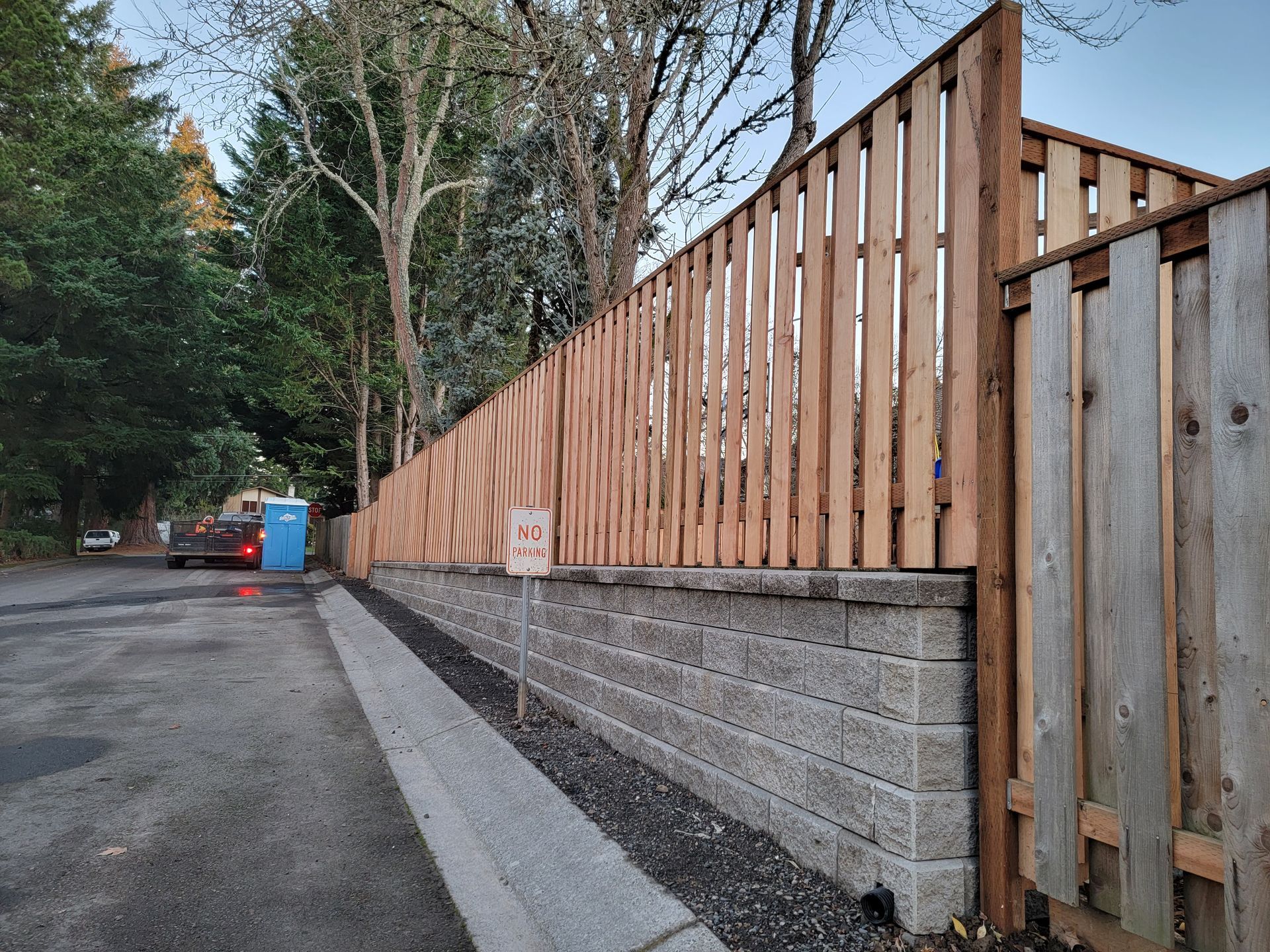 A wooden fence surrounds a brick wall on the side of a road.