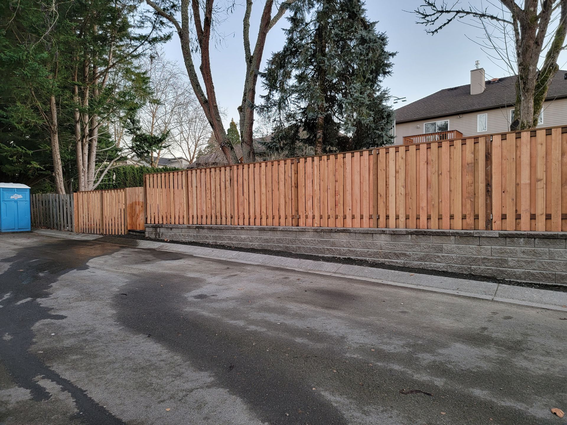 A wooden fence surrounds a parking lot next to a house.