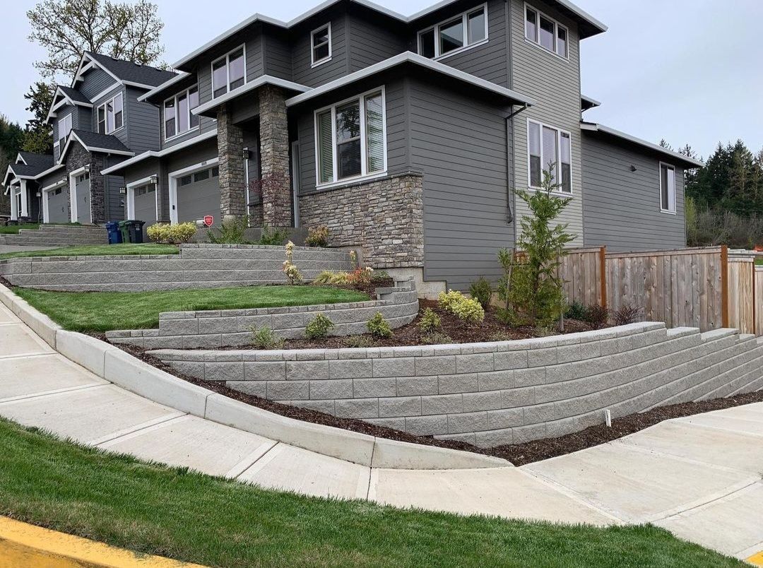 A large house is sitting on top of a hill next to a sidewalk.