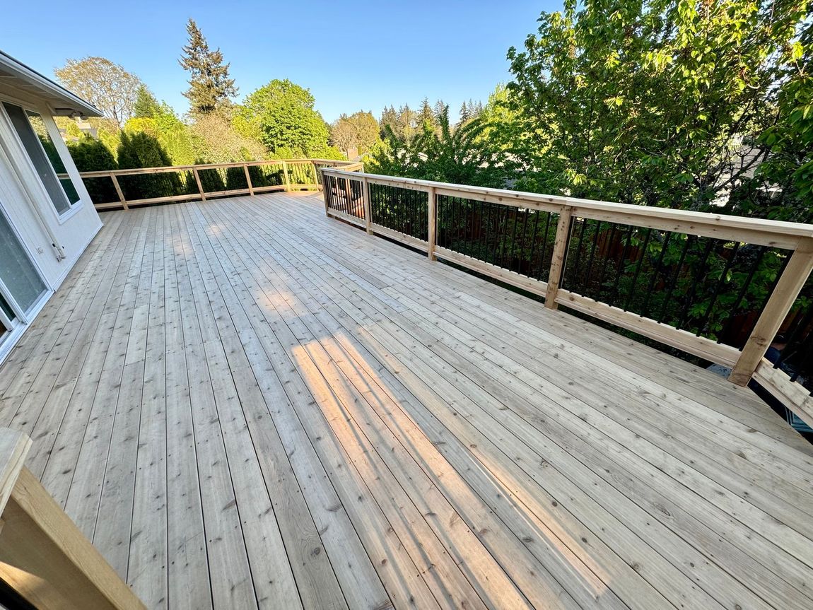 A large wooden deck with a railing and trees in the background